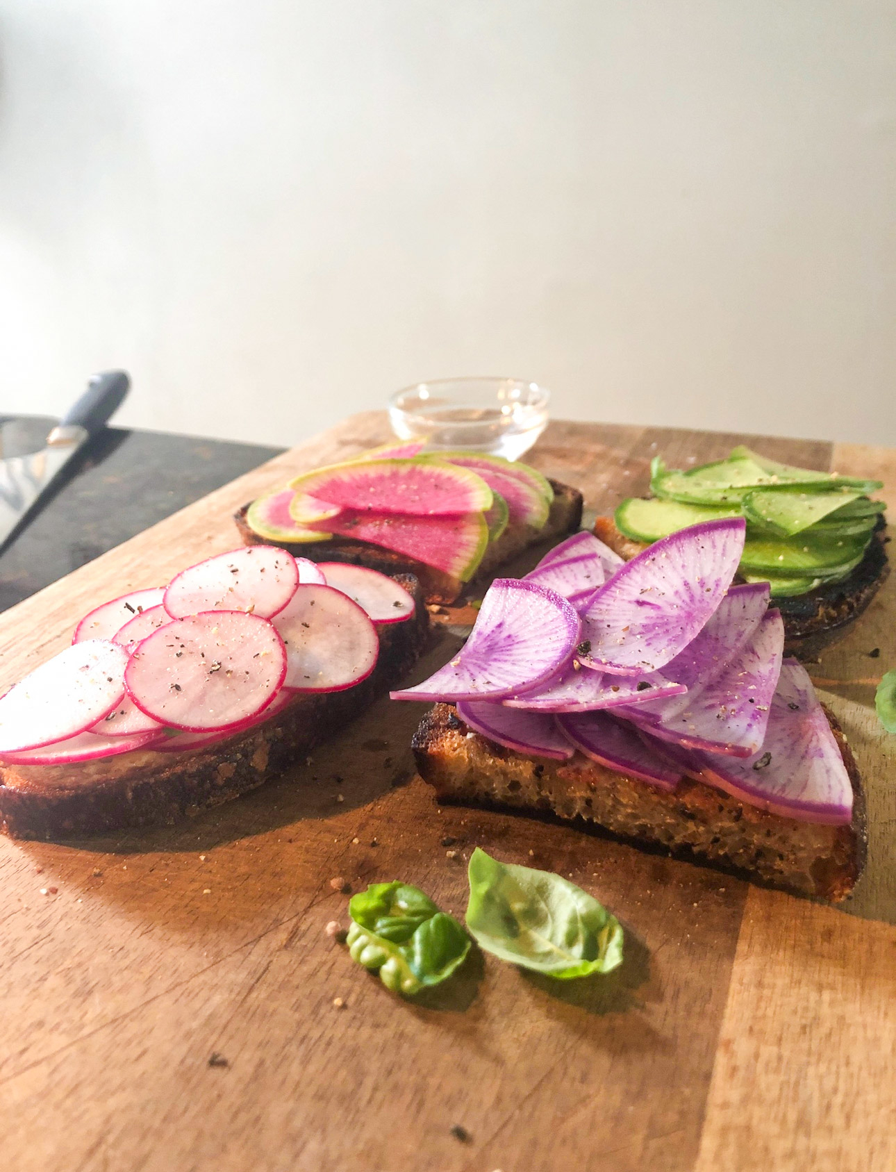Toast with sliced radishes on a wooden board with basil leaves nearby