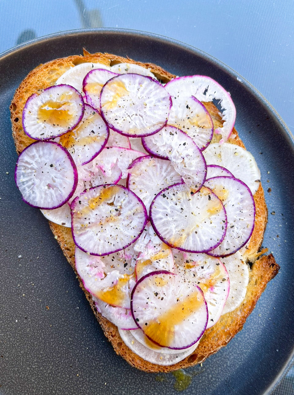 Toast topped with sliced radishes and a drizzle of hot honey on a plate