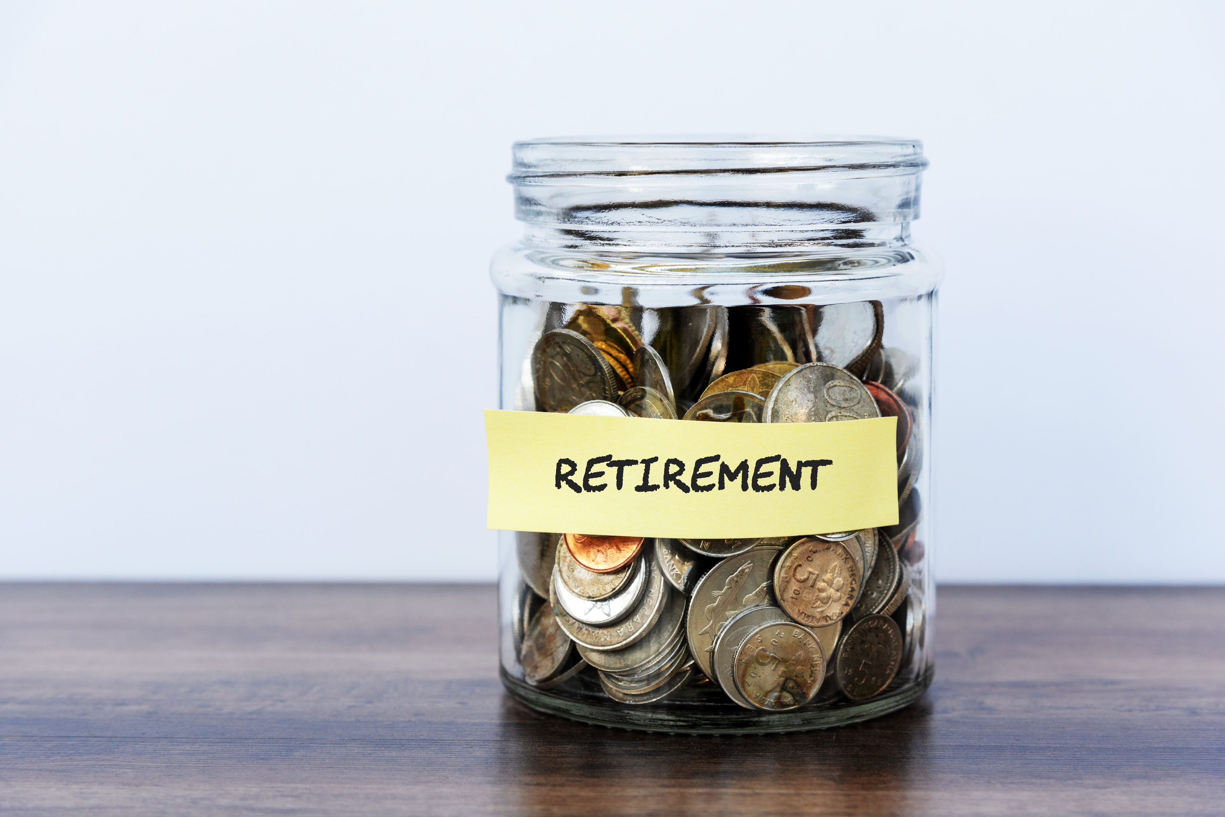 Glass jar filled with coins labeled &quot;RETIREMENT&quot; against a plain background