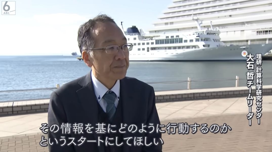 大型クルーズ船の前でインタビューを受けている男性