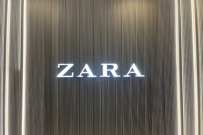 Storefront sign for Zara with illuminated brand name against a background of vertical lines