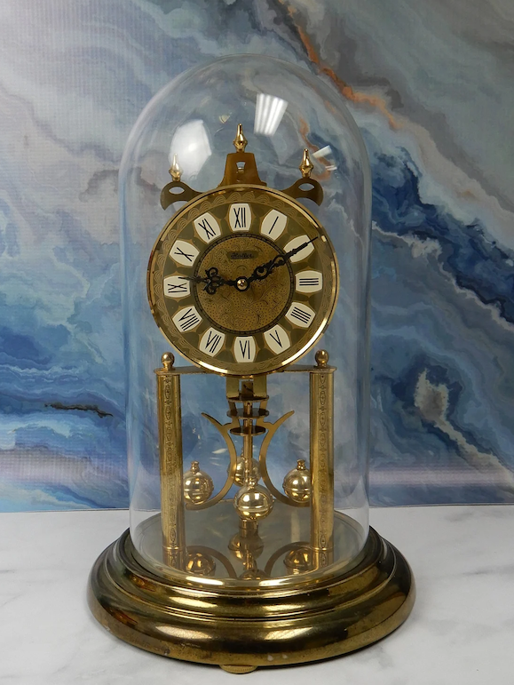 Antique pendulum clock under glass dome on marbled background