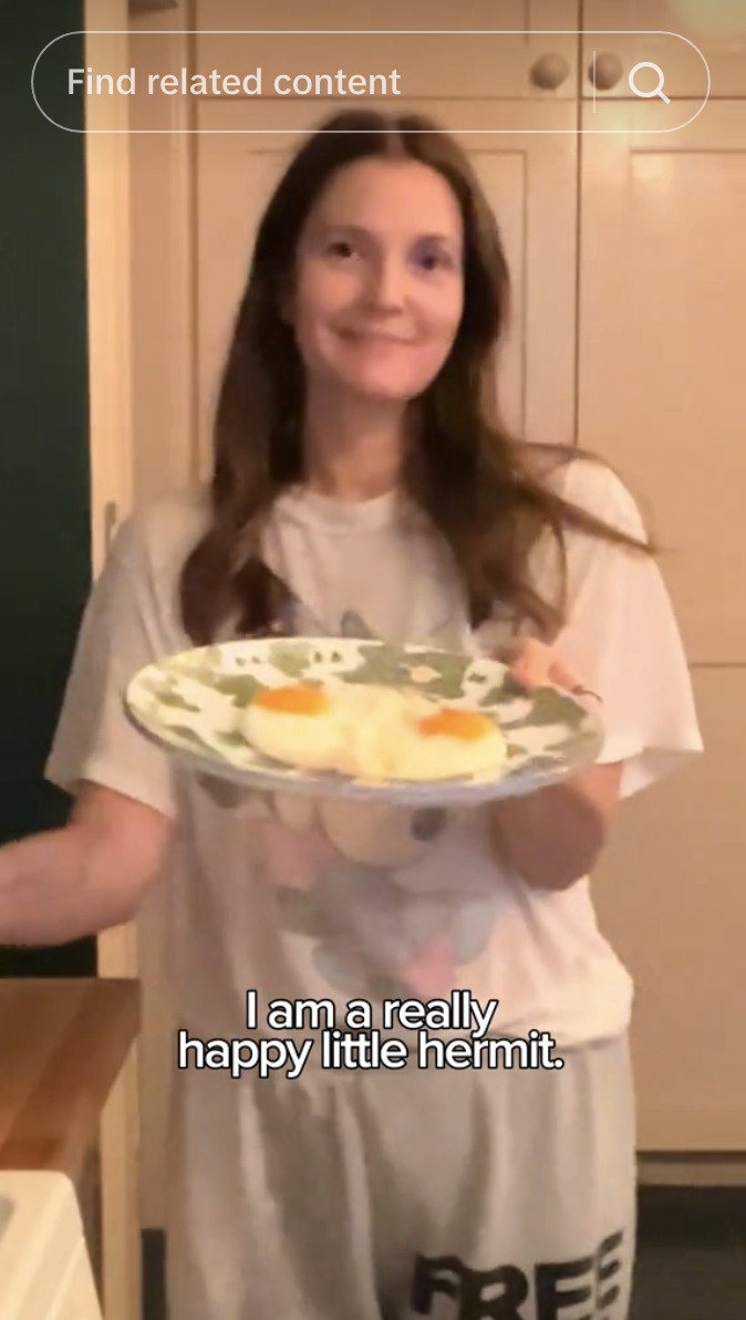 Drew Barrymore smiling and holding a plate of two fried eggs with the caption, &quot;I am really happy hermit&quot;