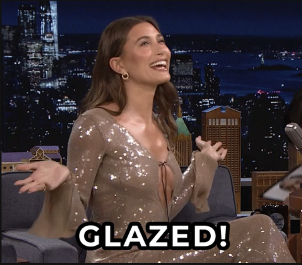 Hailey Bieber in glittery dress laughing on a talk show set with the word &quot;GLAZED!&quot; captioned on the image