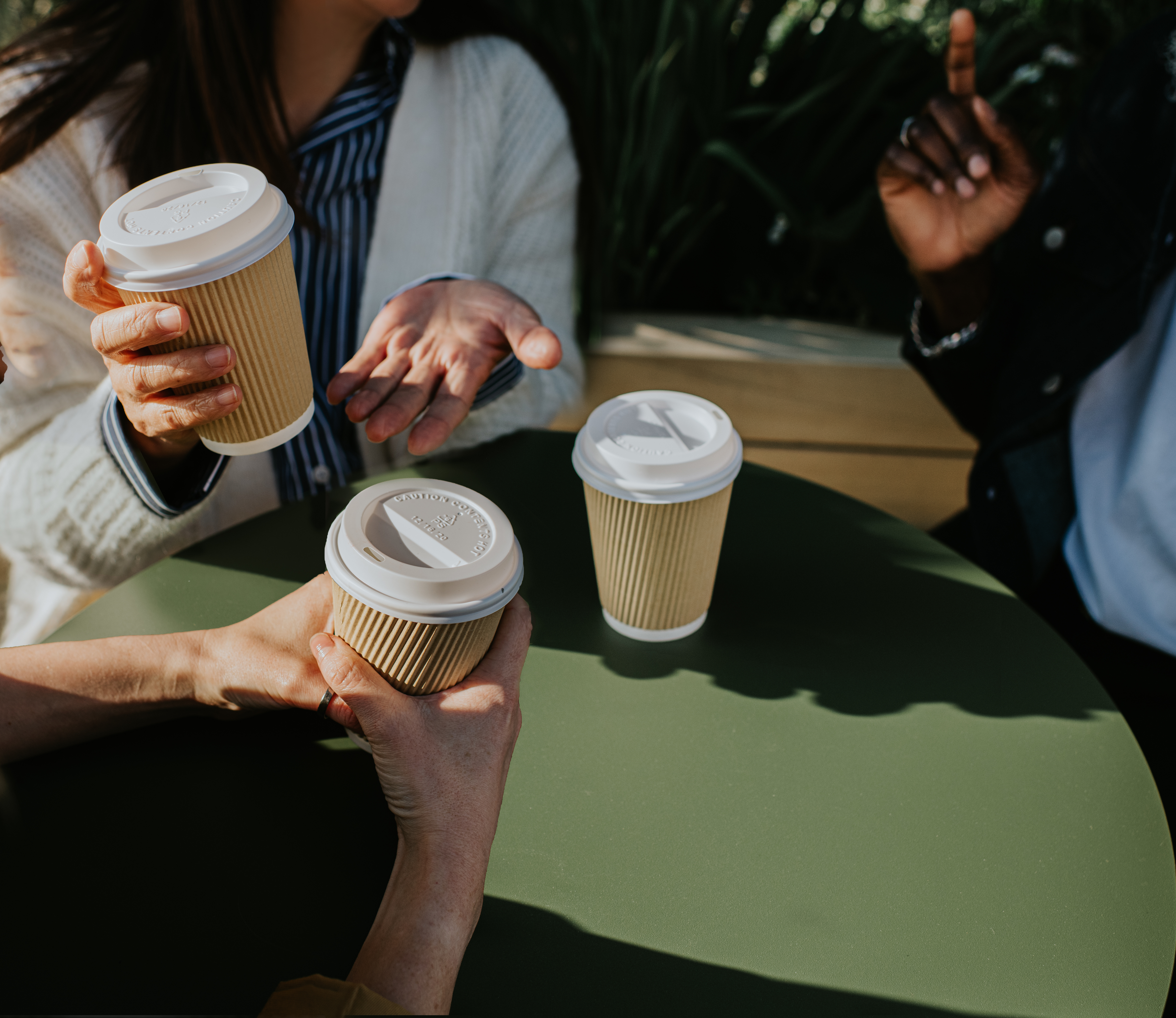 Four people&#x27;s hands, each holding a paper coffee cup over a table, suggesting a social meeting