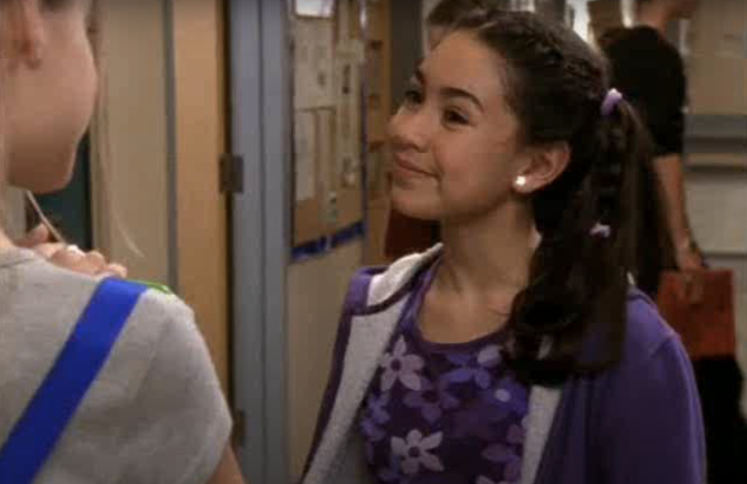 Two characters from a TV show are standing in a school hallway, one facing the camera and the other with a side profile
