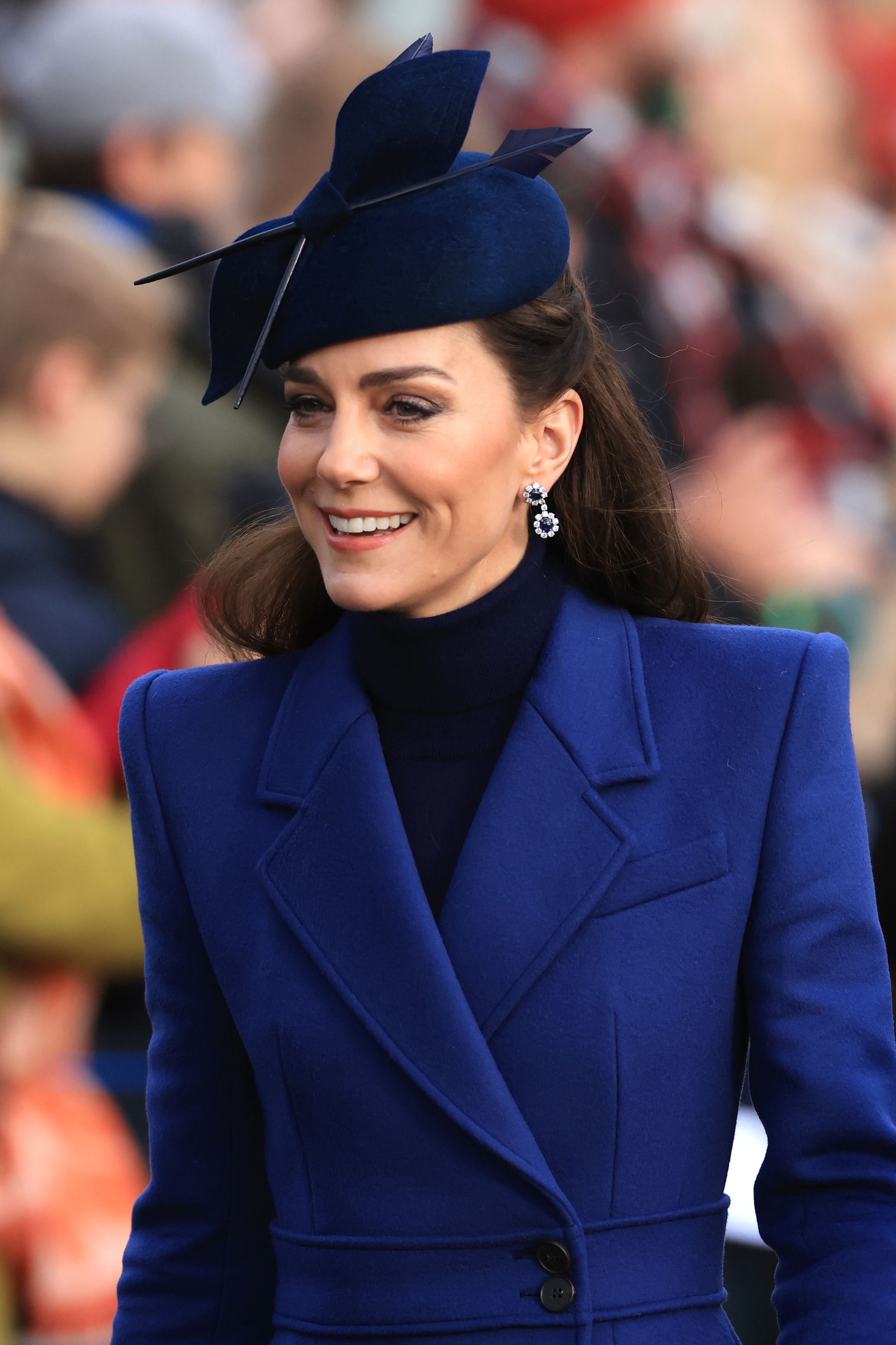 Kate in a structured coat and matching fascinator smiling at an event