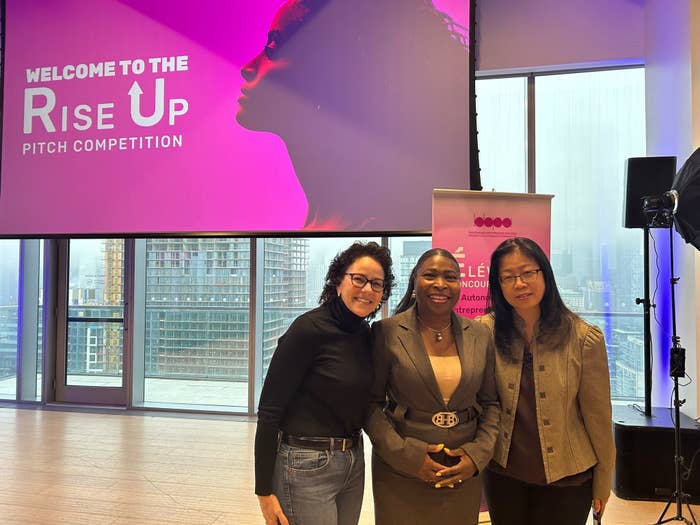 Three women smiling at the &#x27;Rise Up Pitch Competition&#x27; event with cityscape background