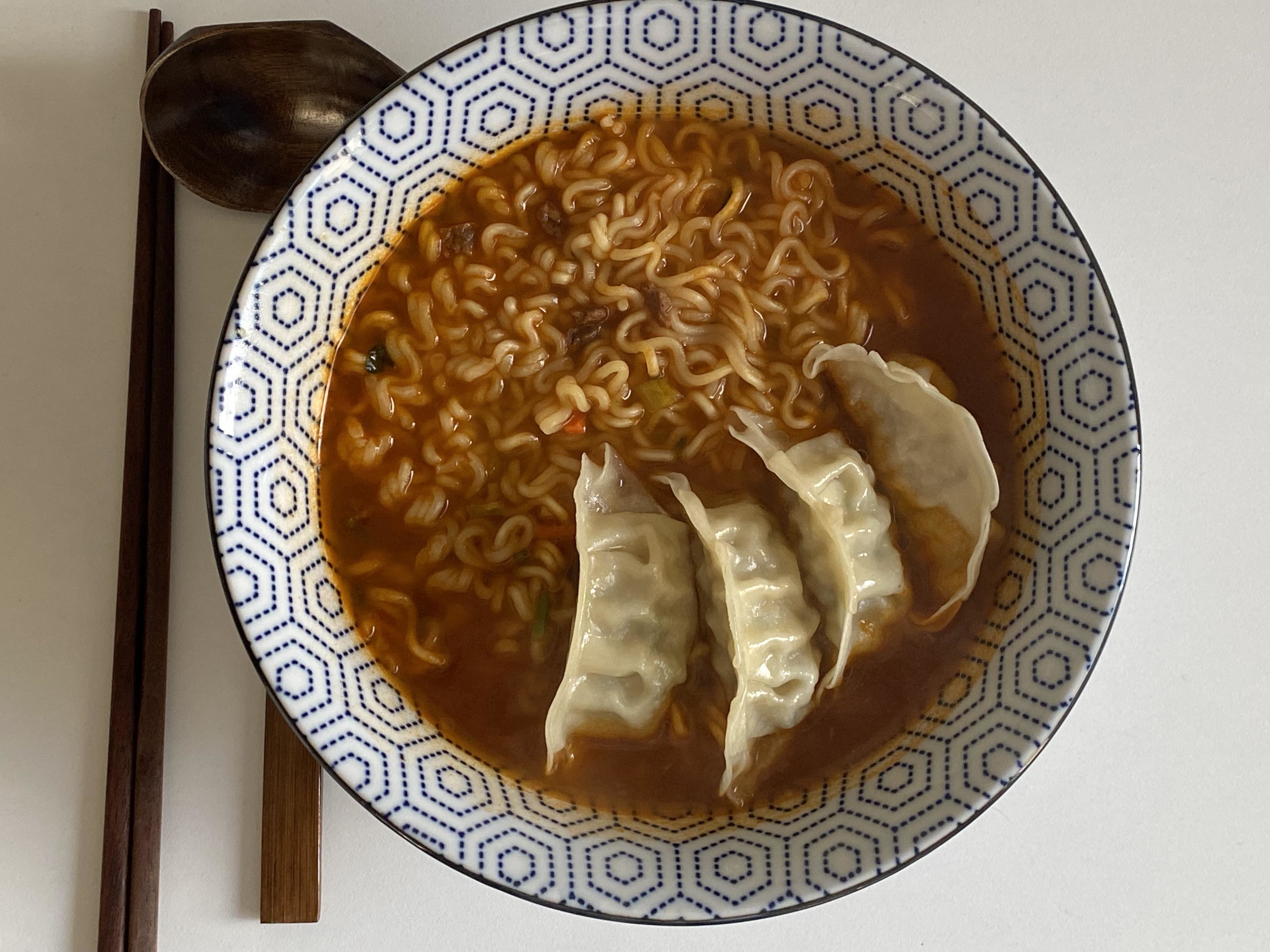Bowl of ramen with three dumplings and a wooden spoon on a patterned border plate