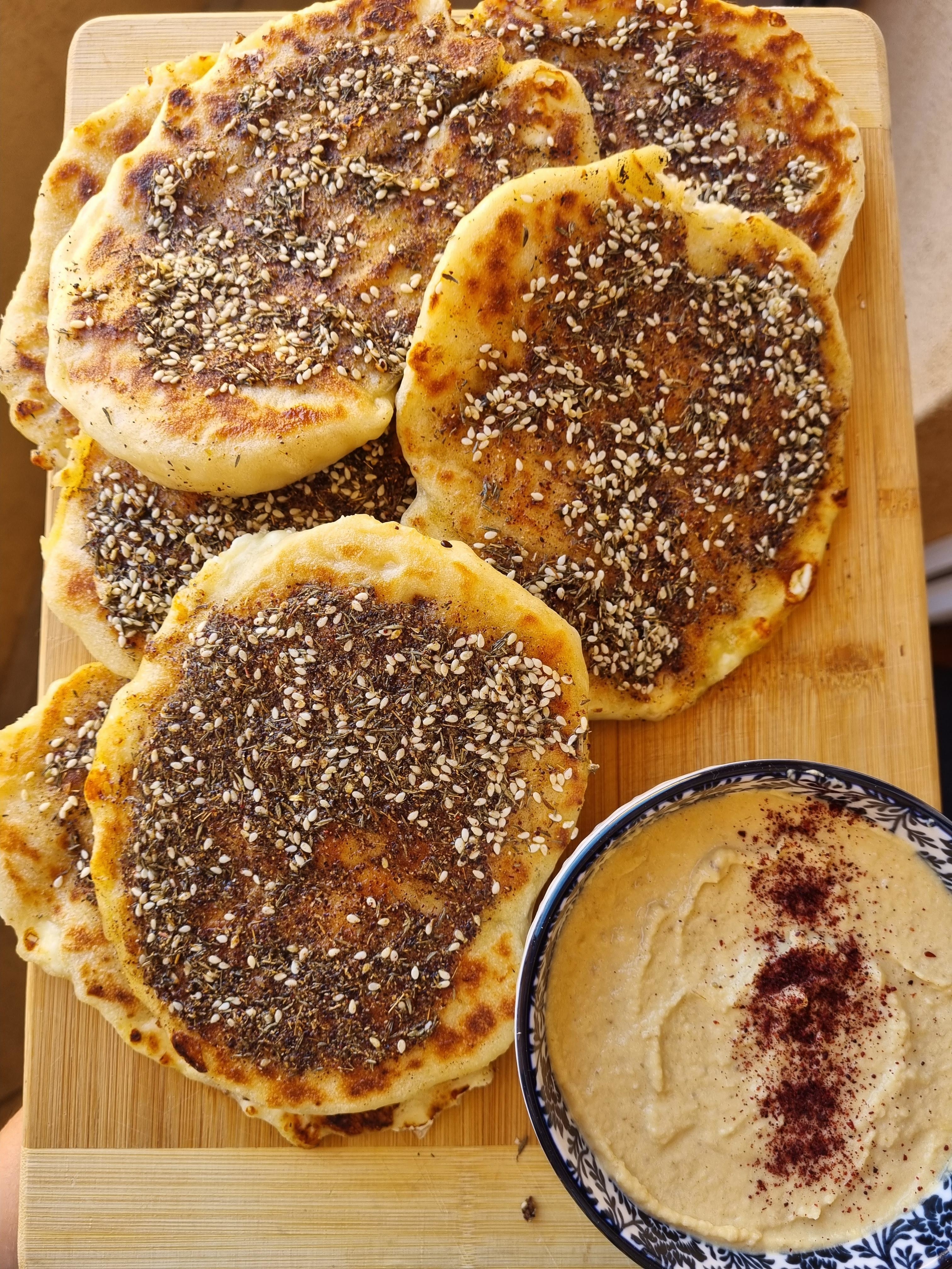 Flatbreads with sesame seeds on a wooden board next to a bowl of dip