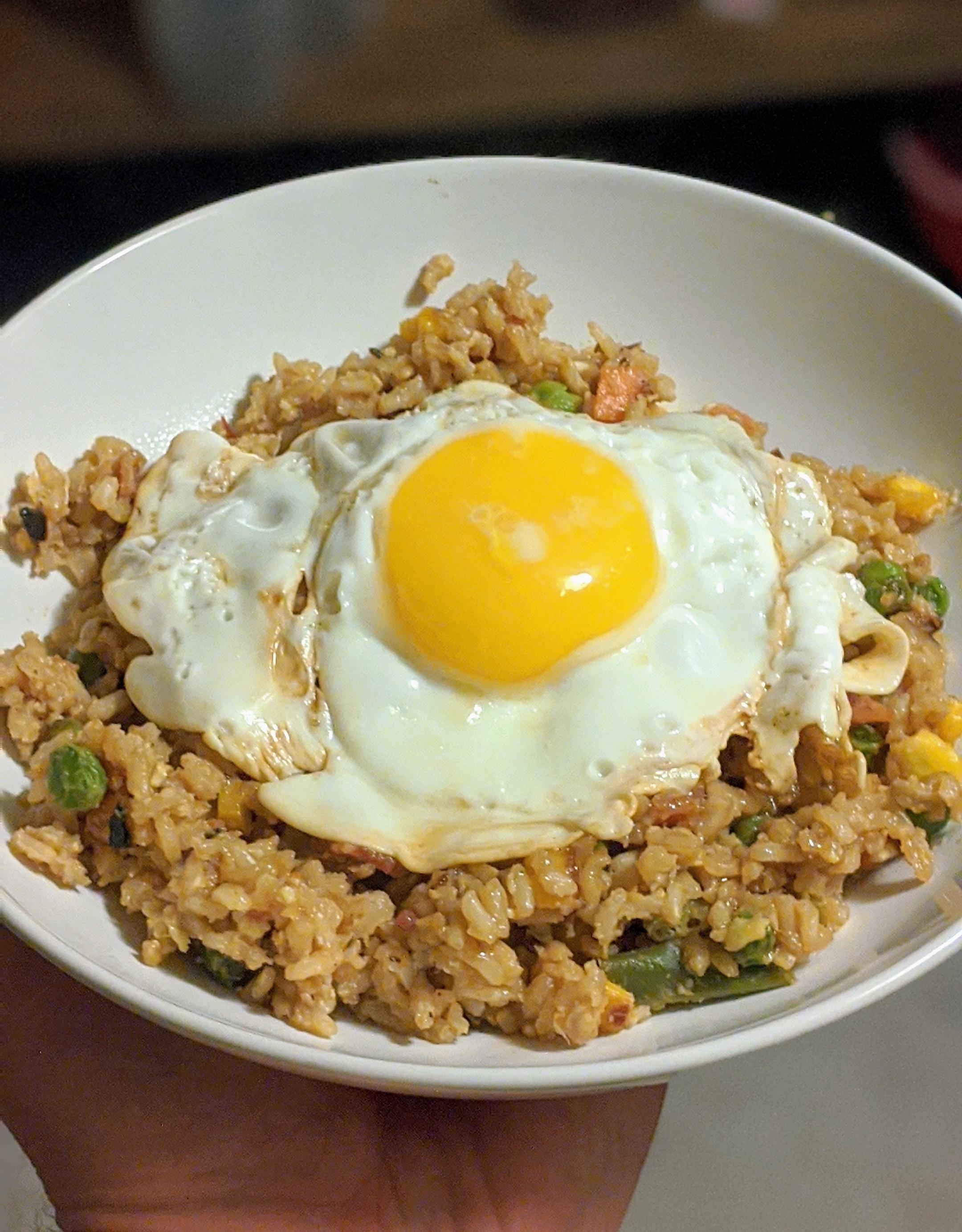 A bowl of fried rice topped with a sunny-side-up egg held in hand