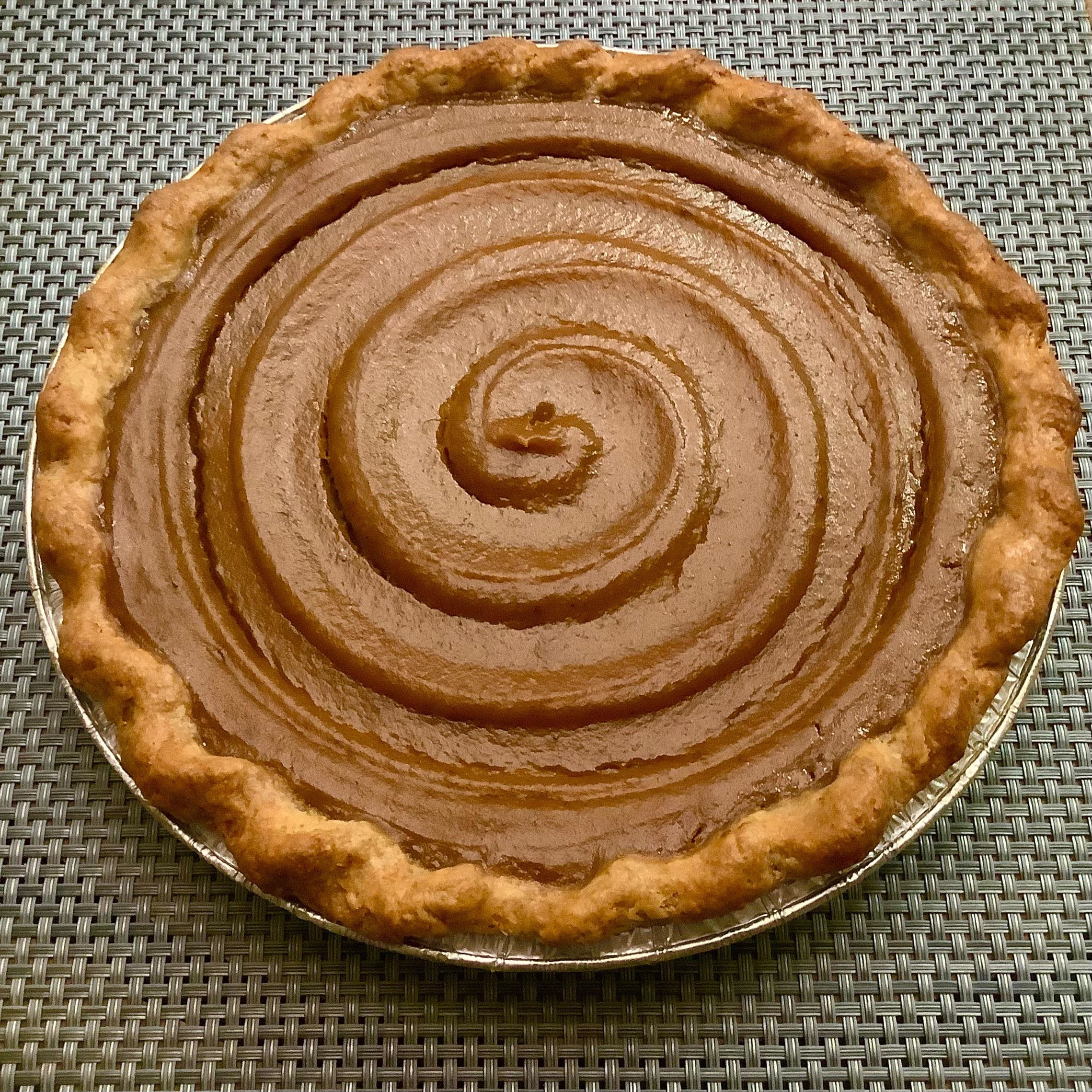 Whole pumpkin pie with a spiral pattern on a textured surface