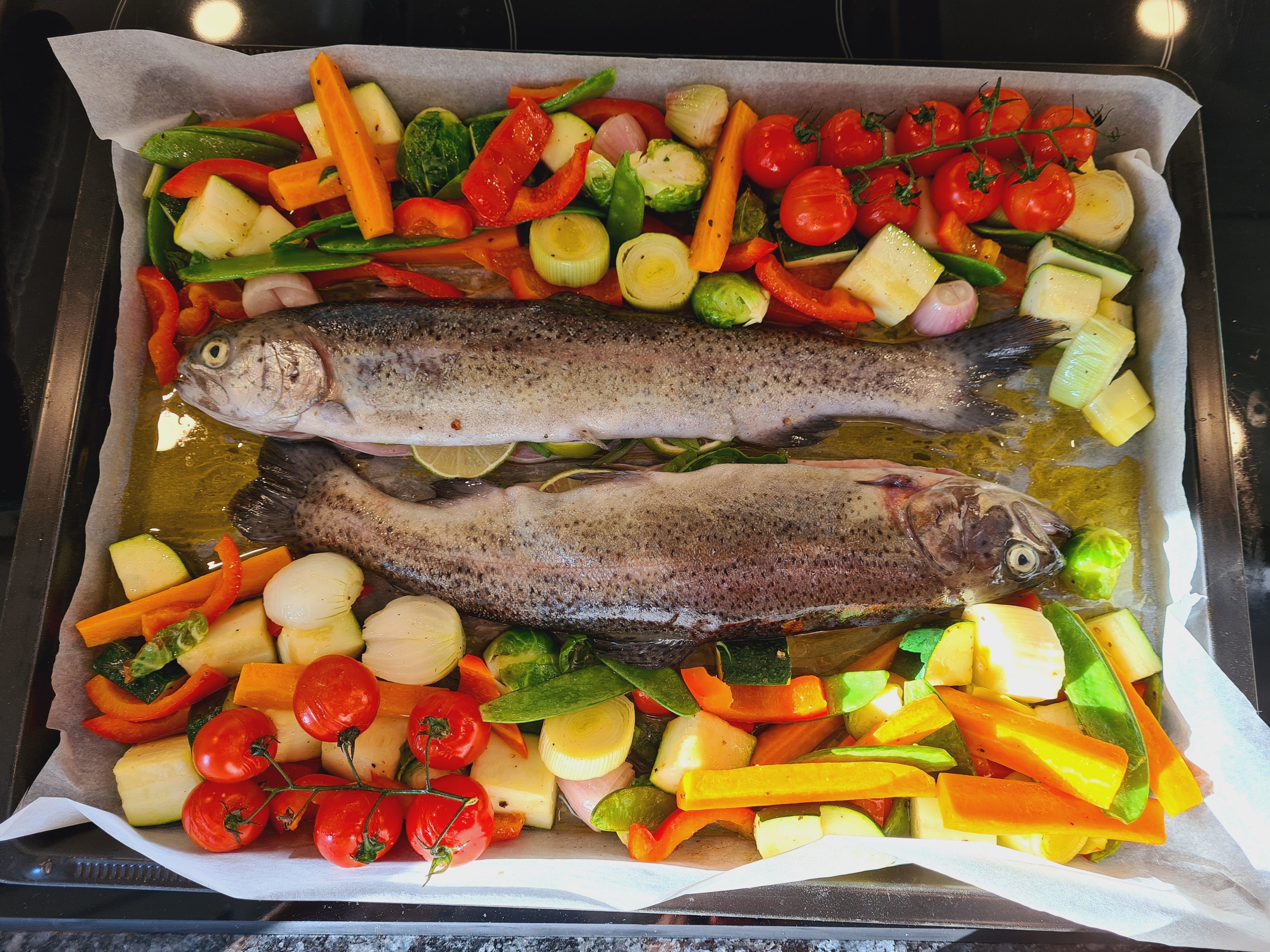 Two fresh whole fish atop a bed of mixed vegetables ready for roasting