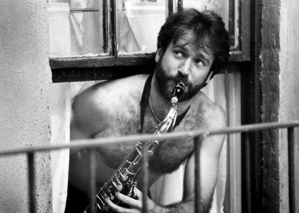Man playing a saxophone behind metal bars, expressing intensity through his performance