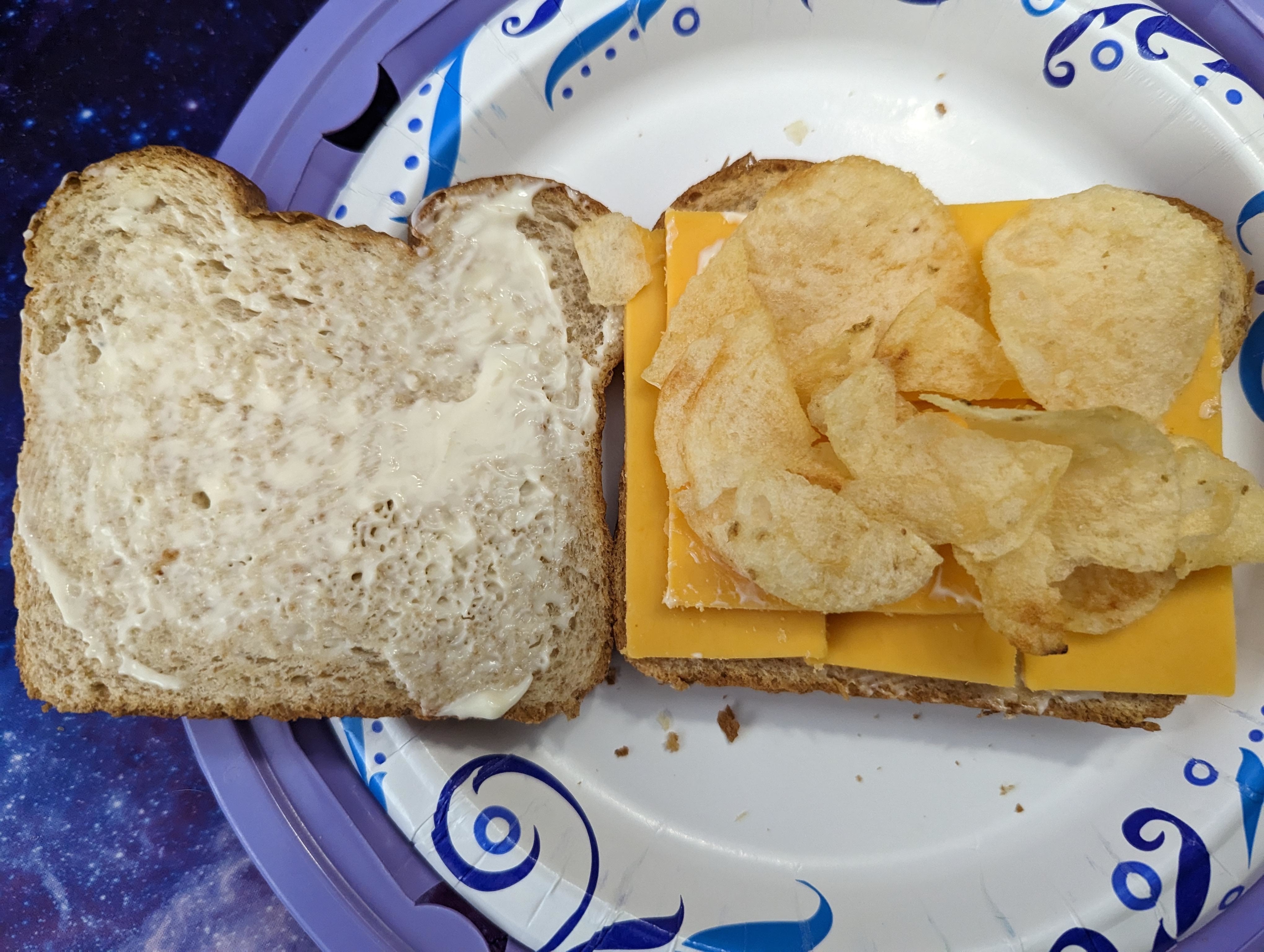 Open-faced sandwich with one slice of bread, mayonnaise, cheese, and potato chips on a paper plate