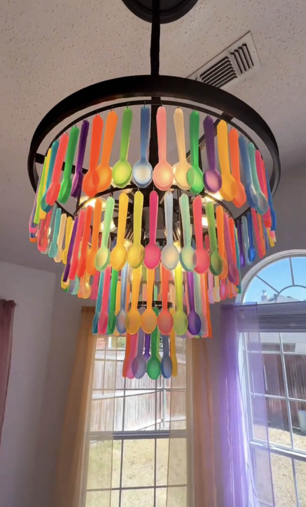 A closer shot of the chandelier made of colorful spoons hanging indoors, creating a unique decoration