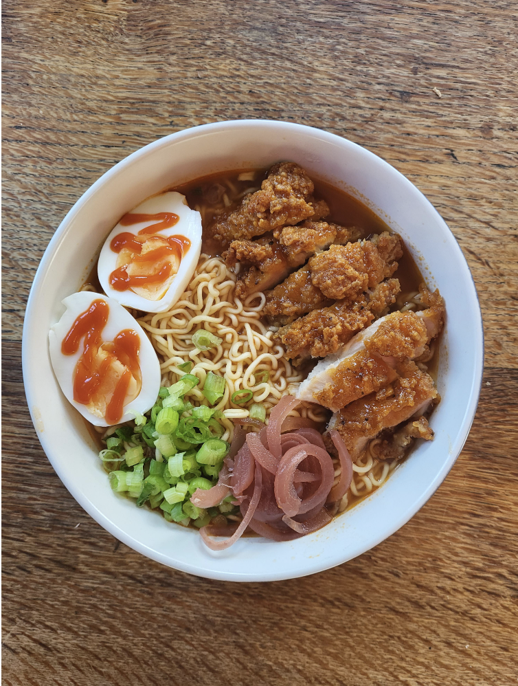 Bowl of ramen with spicy chicken, soft-boiled egg, green onions, and pickled ginger on wood table