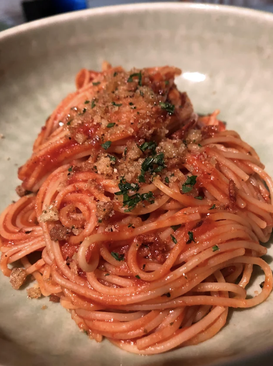 A plate of spaghetti with tomato sauce and a sprinkling of herbs and breadcrumbs