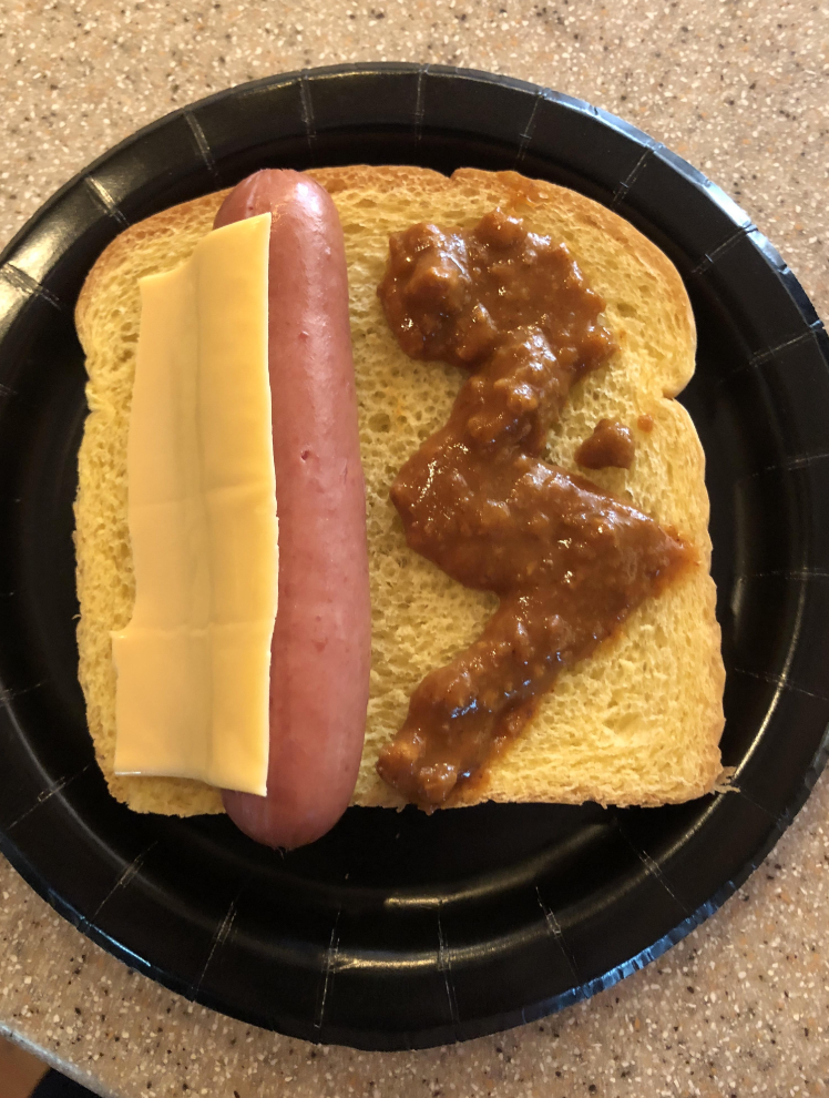 A hotdog with a slice of cheese on a piece of bread, topped with a scoop of sauce, on a black plate