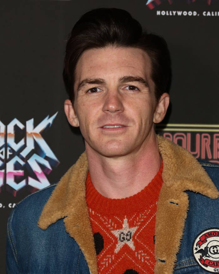 A closeup of drake bell in a denim jacket and patterned sweater at an event