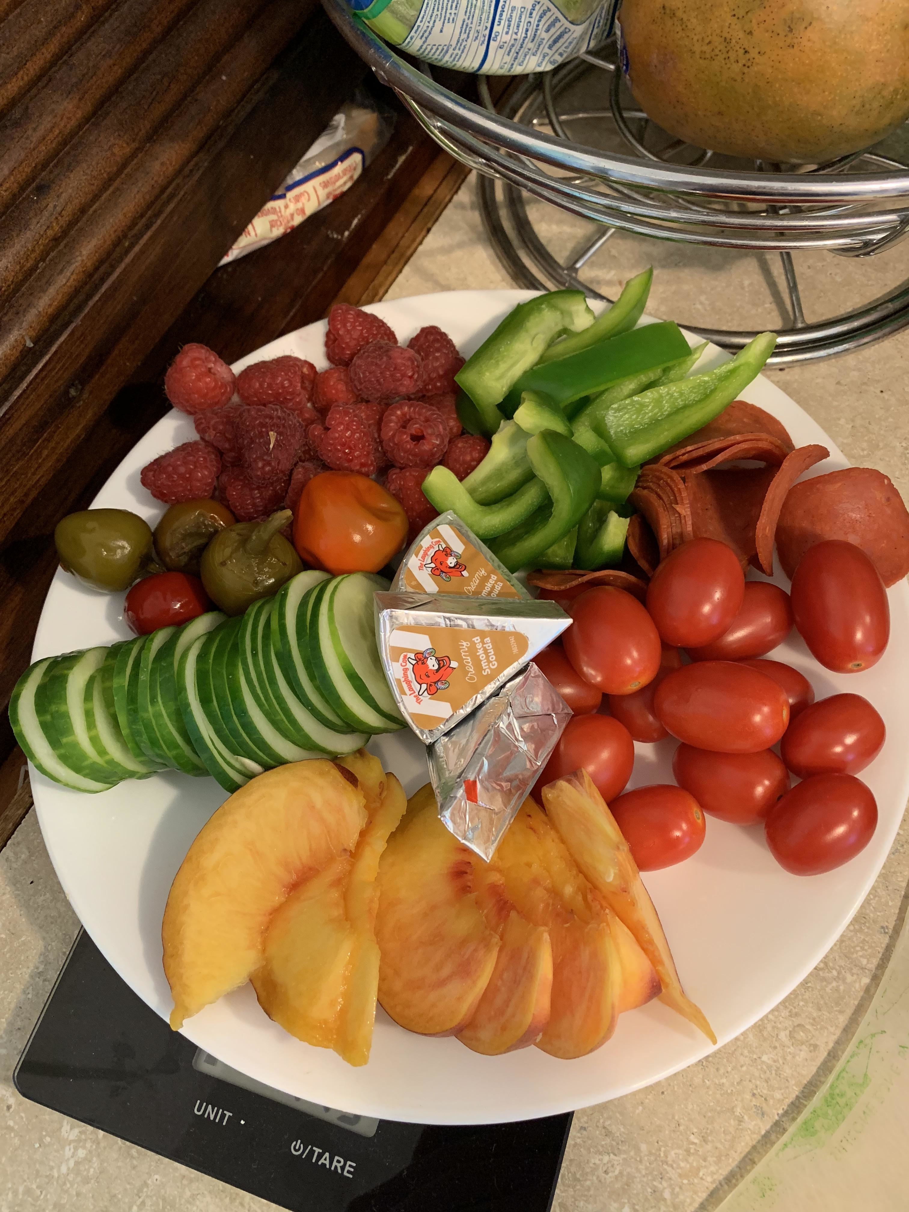 Assorted fresh sliced fruits and vegetables displayed on a plate with a pack of dipping sauce in the center