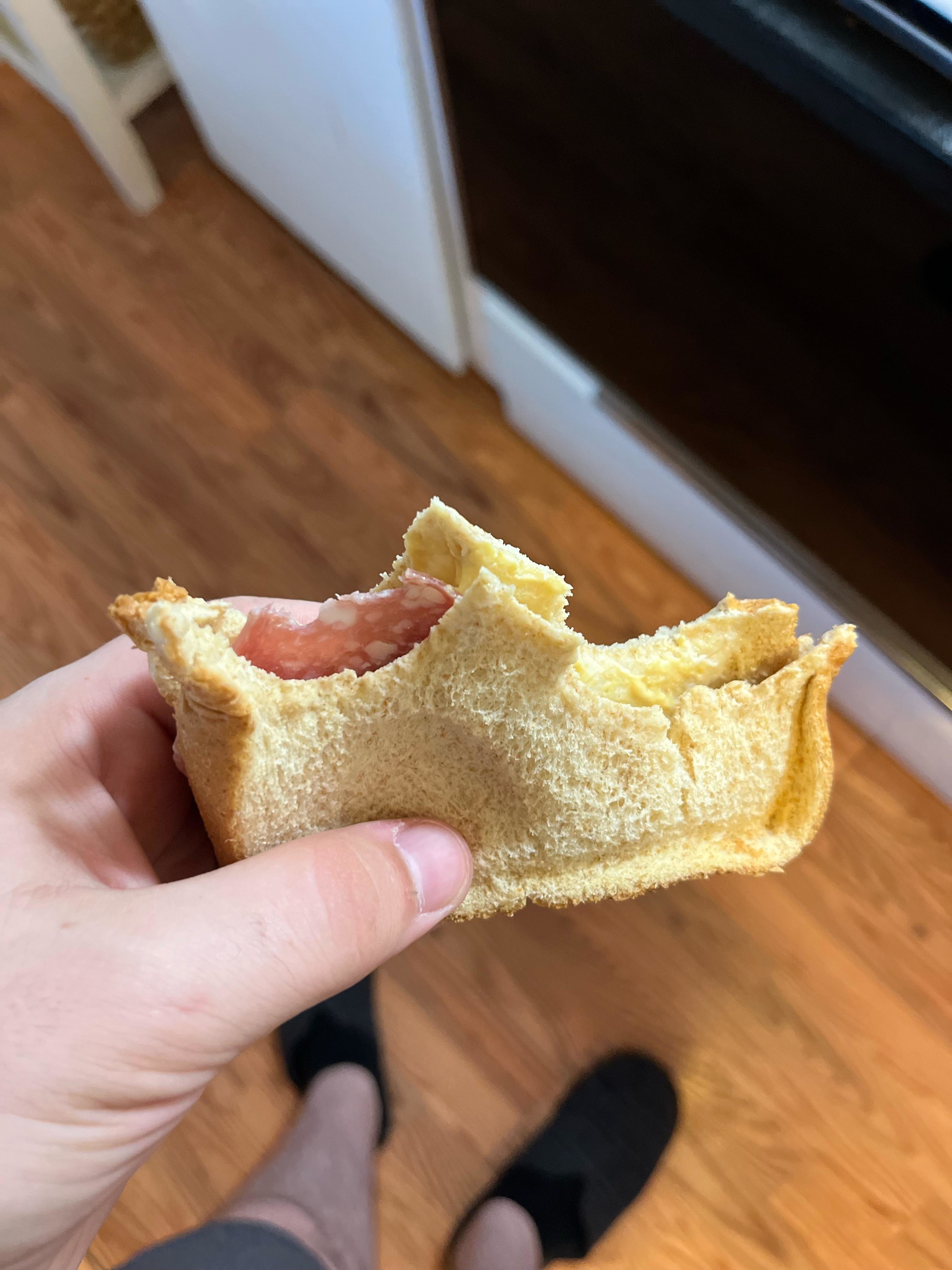 Person holding a bitten sandwich with visible sausage filling