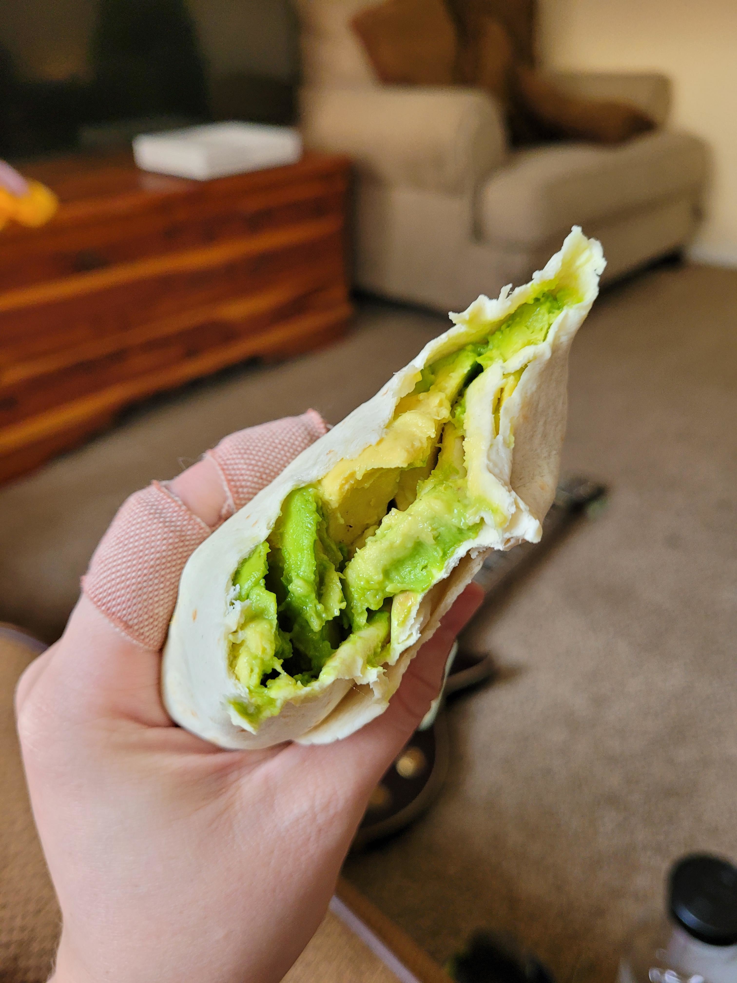 Hand holding a half-eaten avocado wrap indoors