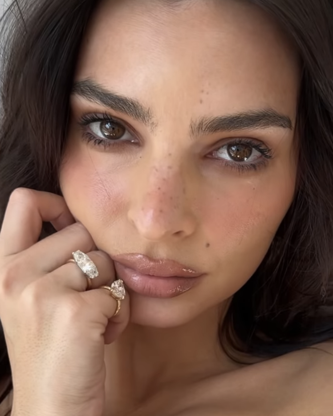 Close-up of Emily Ratajkowski with light makeup, resting her chin on her hand adorned with rings