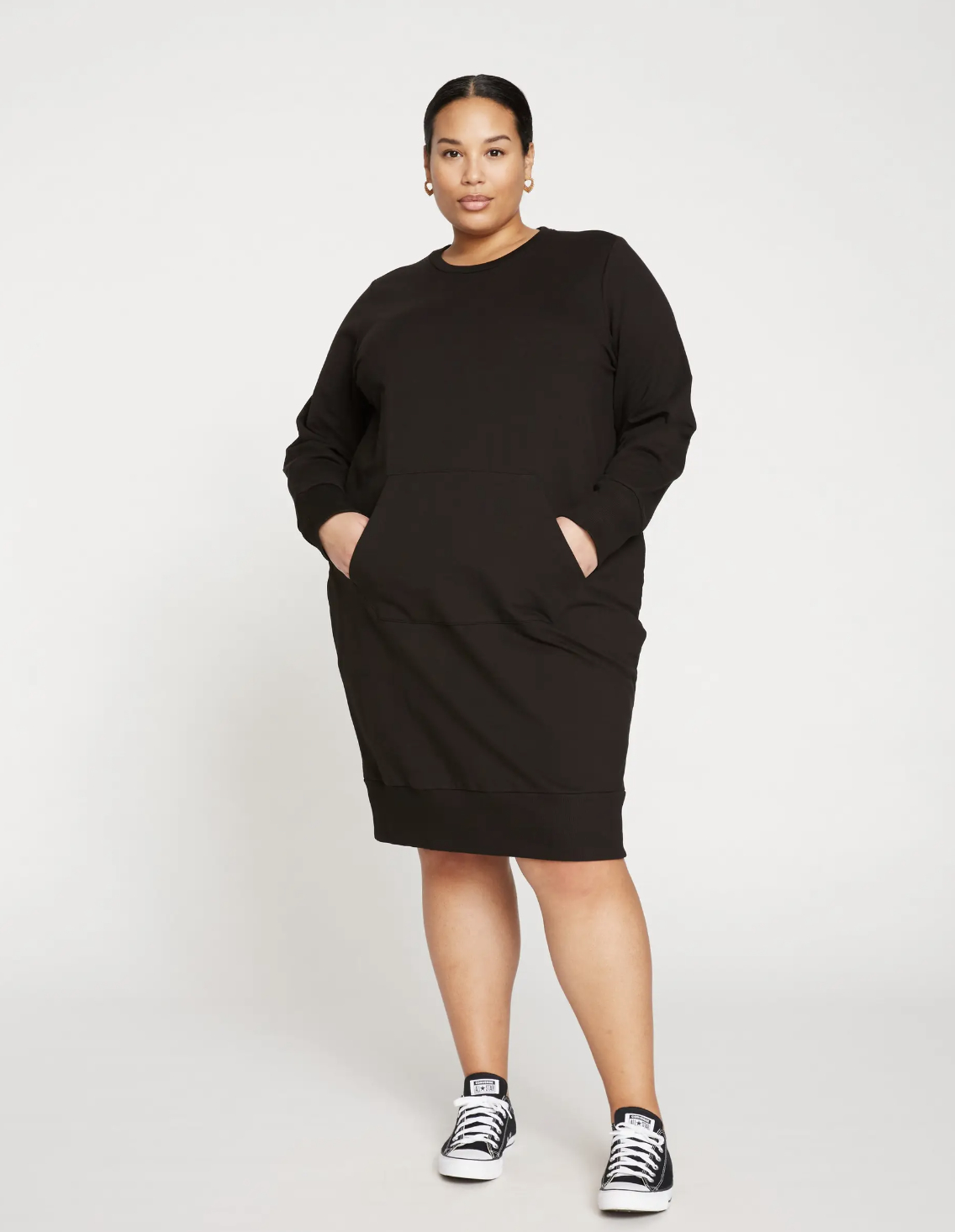 Woman in a casual black dress with pockets, paired with sneakers, poses for a shopping feature