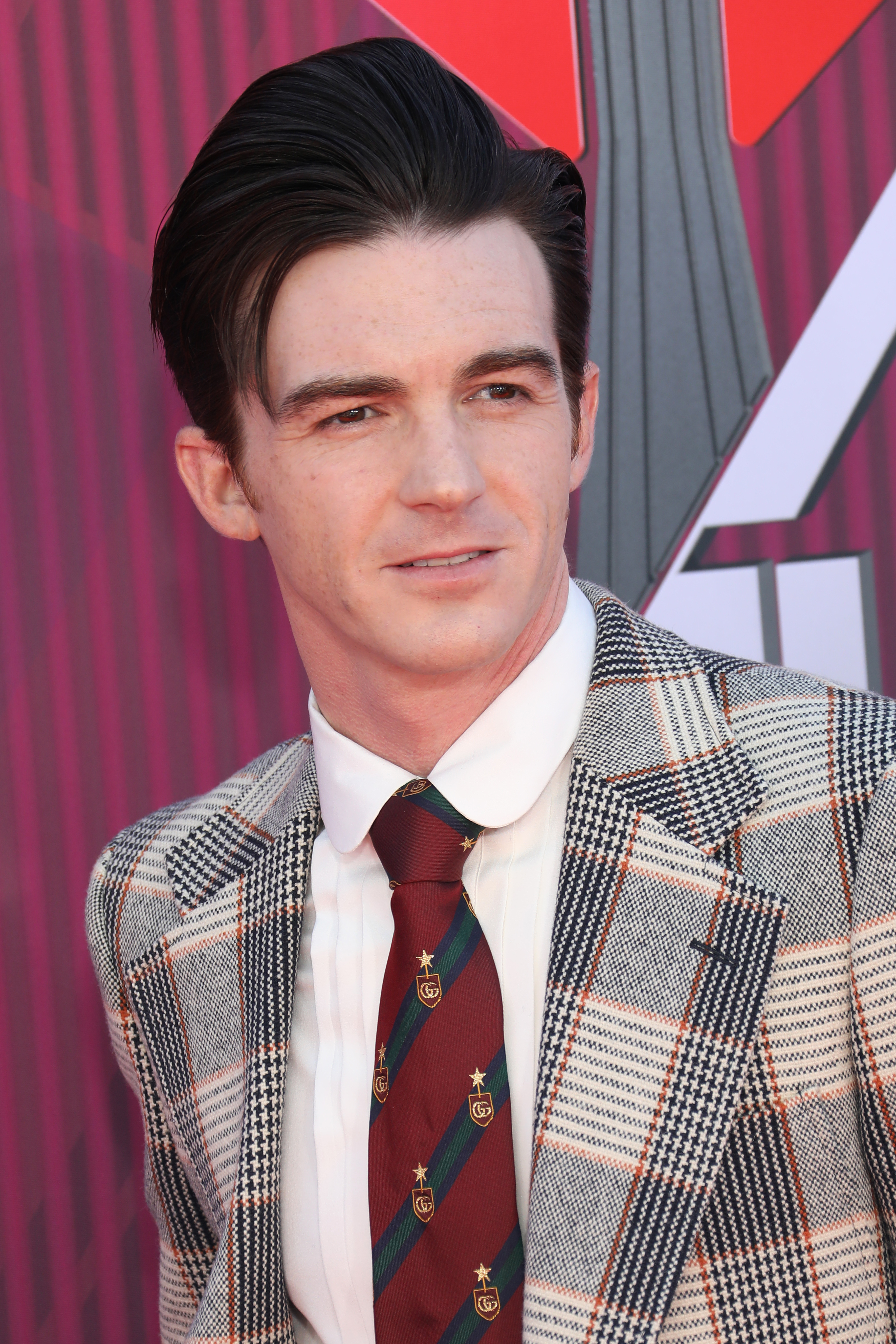 Drake Bell at an event, wearing a plaid suit with a striped tie and a collared shirt
