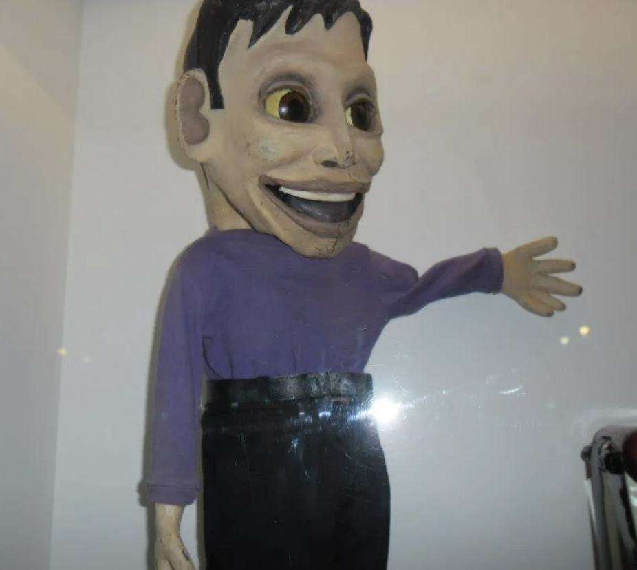 Handmade puppet with exaggerated facial features, wearing a purple top and black bottom, displayed in a case