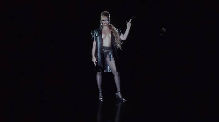 Beyoncé in an edgy open jacket with no shirt underneath and high heels holding  her fingers up as if they are a pistol in a shot from &quot;Texas Hold &#x27;Em&quot;
