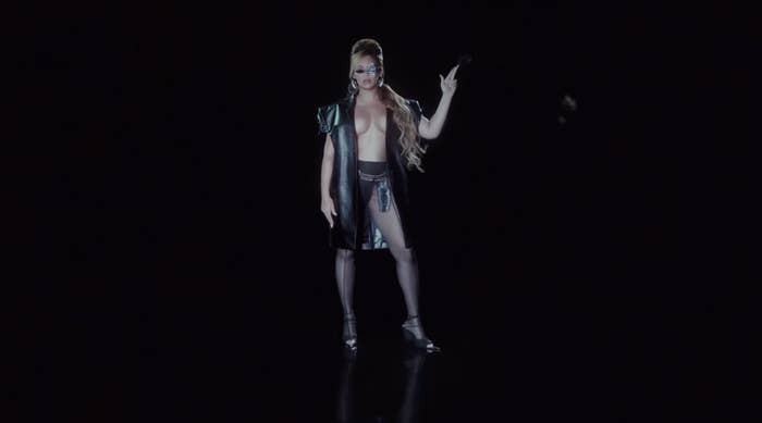 Beyoncé in an edgy open jacket with no shirt underneath and high heels holding her fingers up as if they are a pistol in a shot from "Texas Hold 'Em"