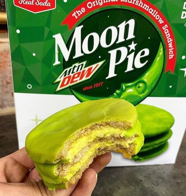 Hand holding a partially eaten Moon Pie with a Mtn Dew flavor, packaging in background