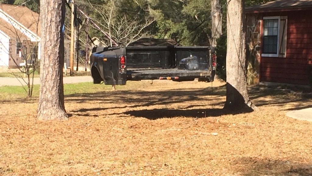 Car suspended in air between two trees, rear-end damaged, near a house. No persons visible
