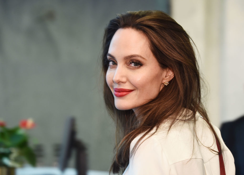 Angelina posing sideways, glancing at the camera with a soft smile, wearing a stylish blouse