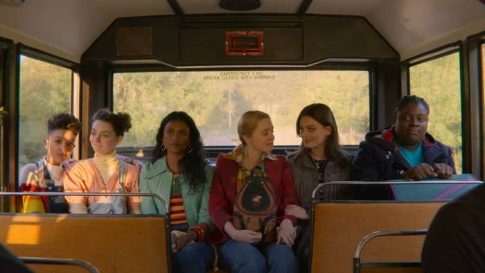 Group of six women sitting in a bus, looking forward with varying expressions