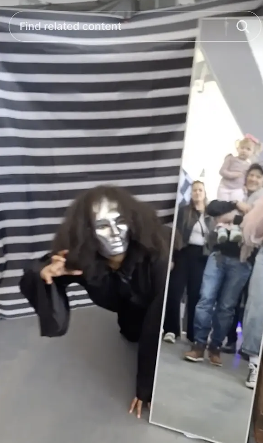 Person in a black outfit with silver face paint posing in front of a striped backdrop