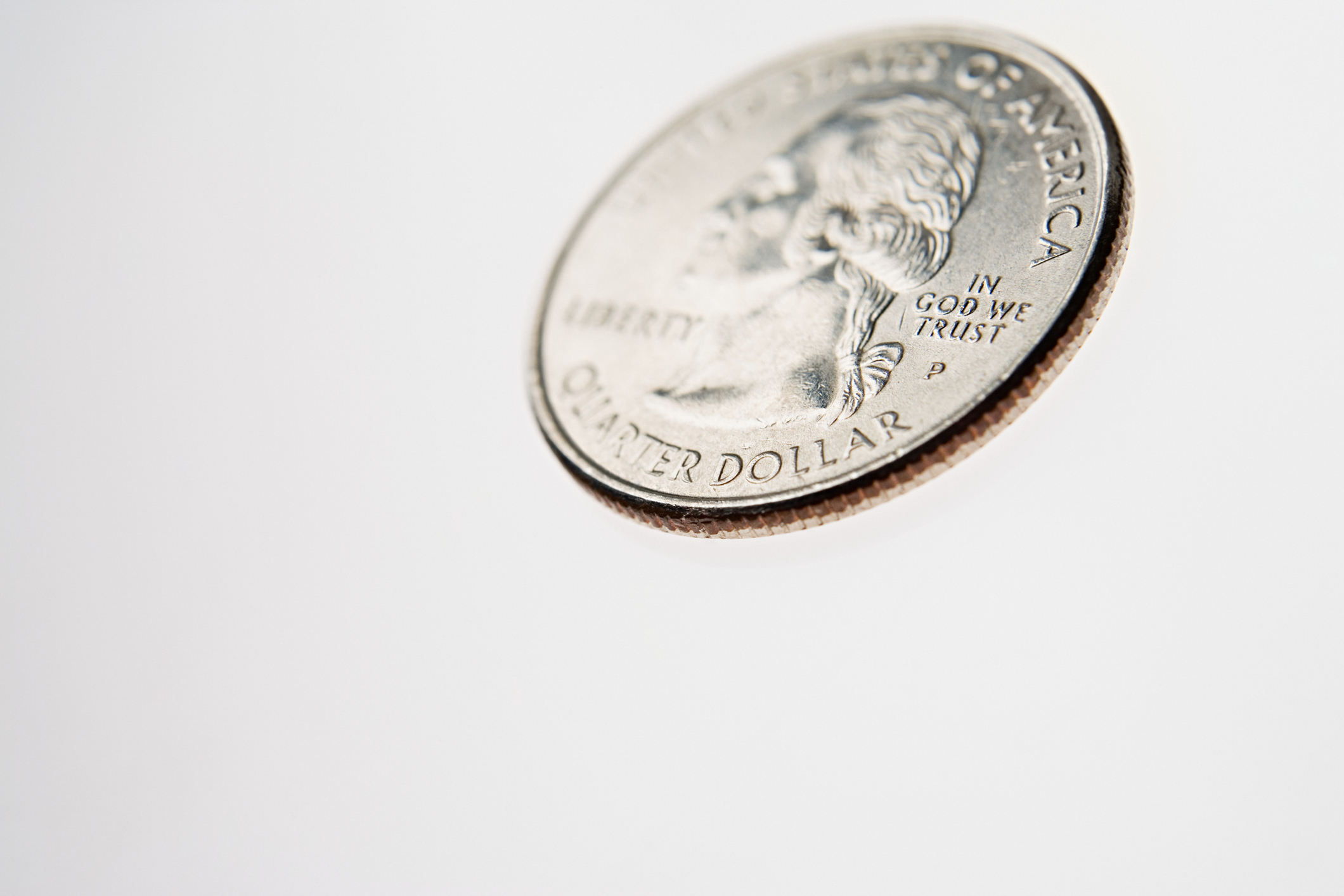 A close-up of a quarter tilted on a white surface, showing part of George Washington&#x27;s profile