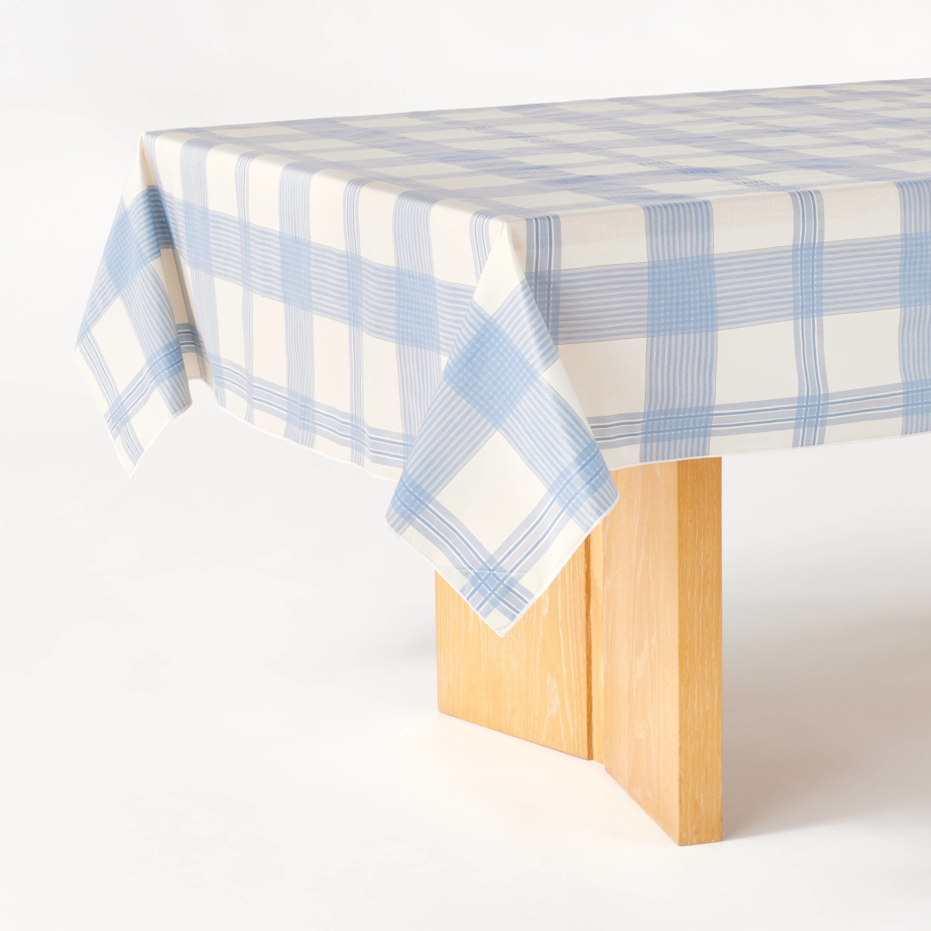 A corner of a wooden table with a blue and white checkered tablecloth hanging off the edge