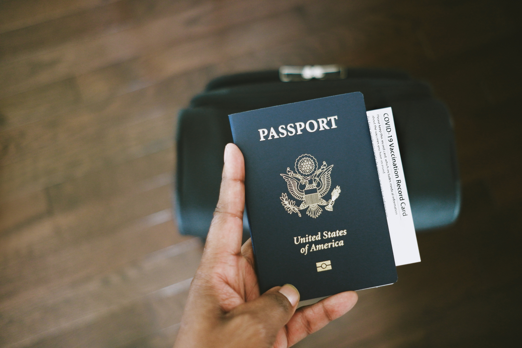 Hand holding a US passport over a suitcase, suggesting travel preparation