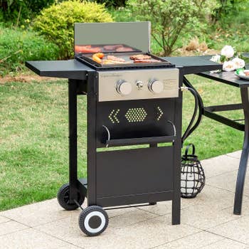 Portable grill in a garden with food cooking on it next to a dining table
