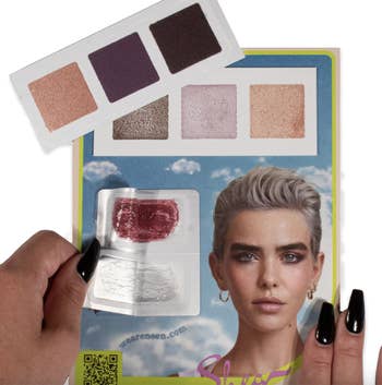Hands holding a cosmetics brochure and eyeshadow palette with a model sporting a bold makeup look