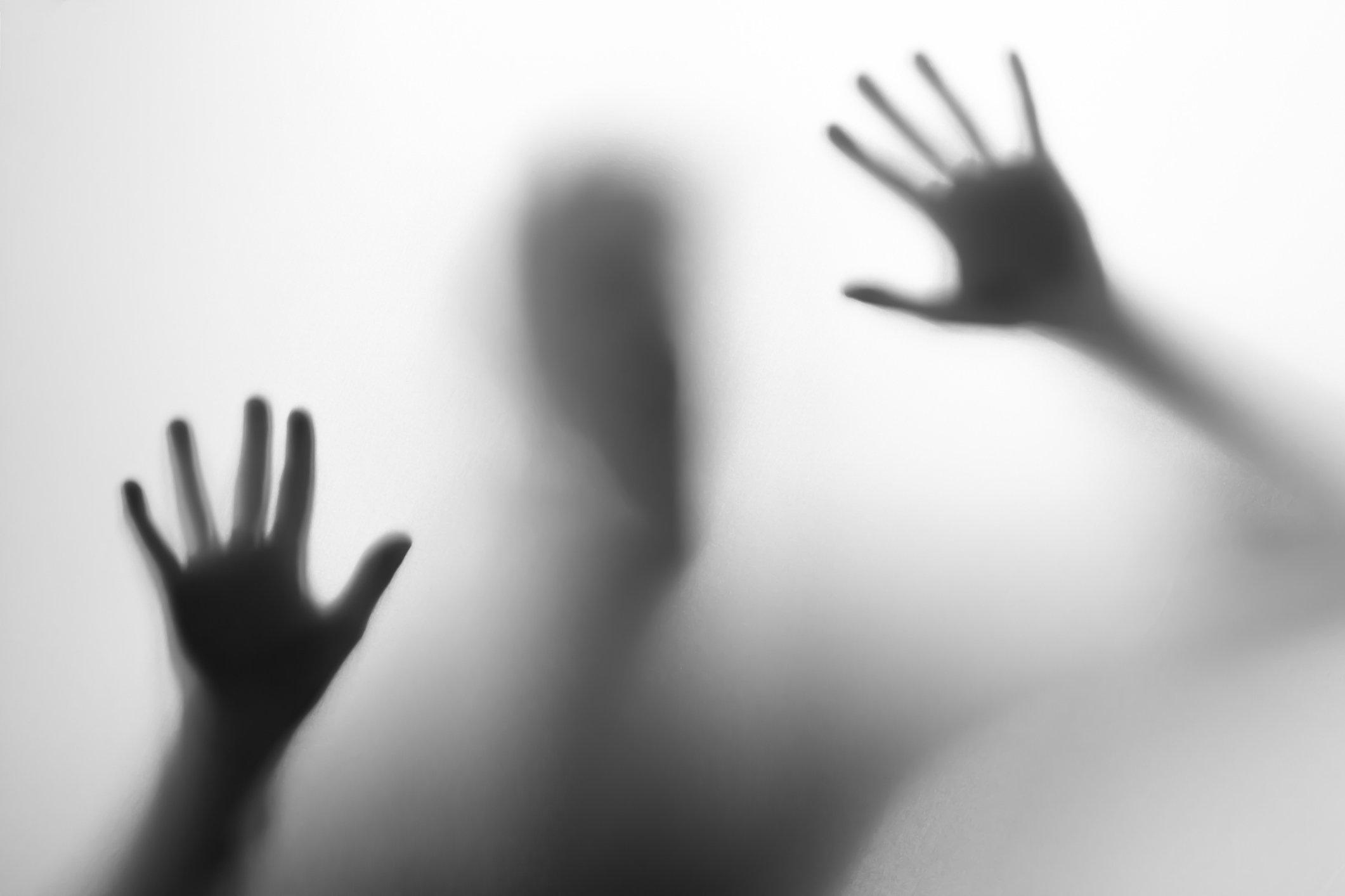 Shadow of hands pressed against opaque surface, evoking mystery in a monochrome setting