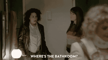 Three characters from a TV show appear in a tense scene, one character asking about the bathroom location