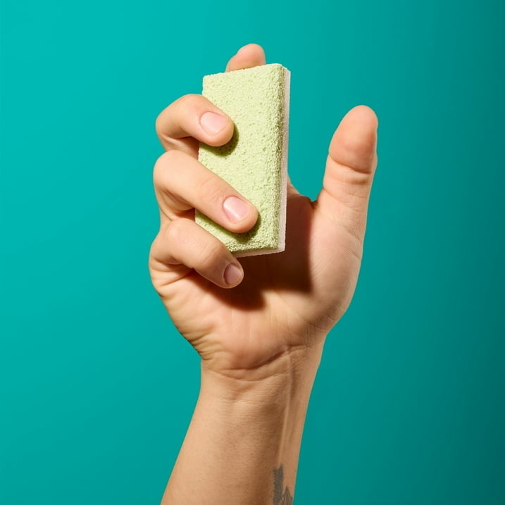 Hand holding a green sponge against a plain background, highlighting the product for shopping purposes