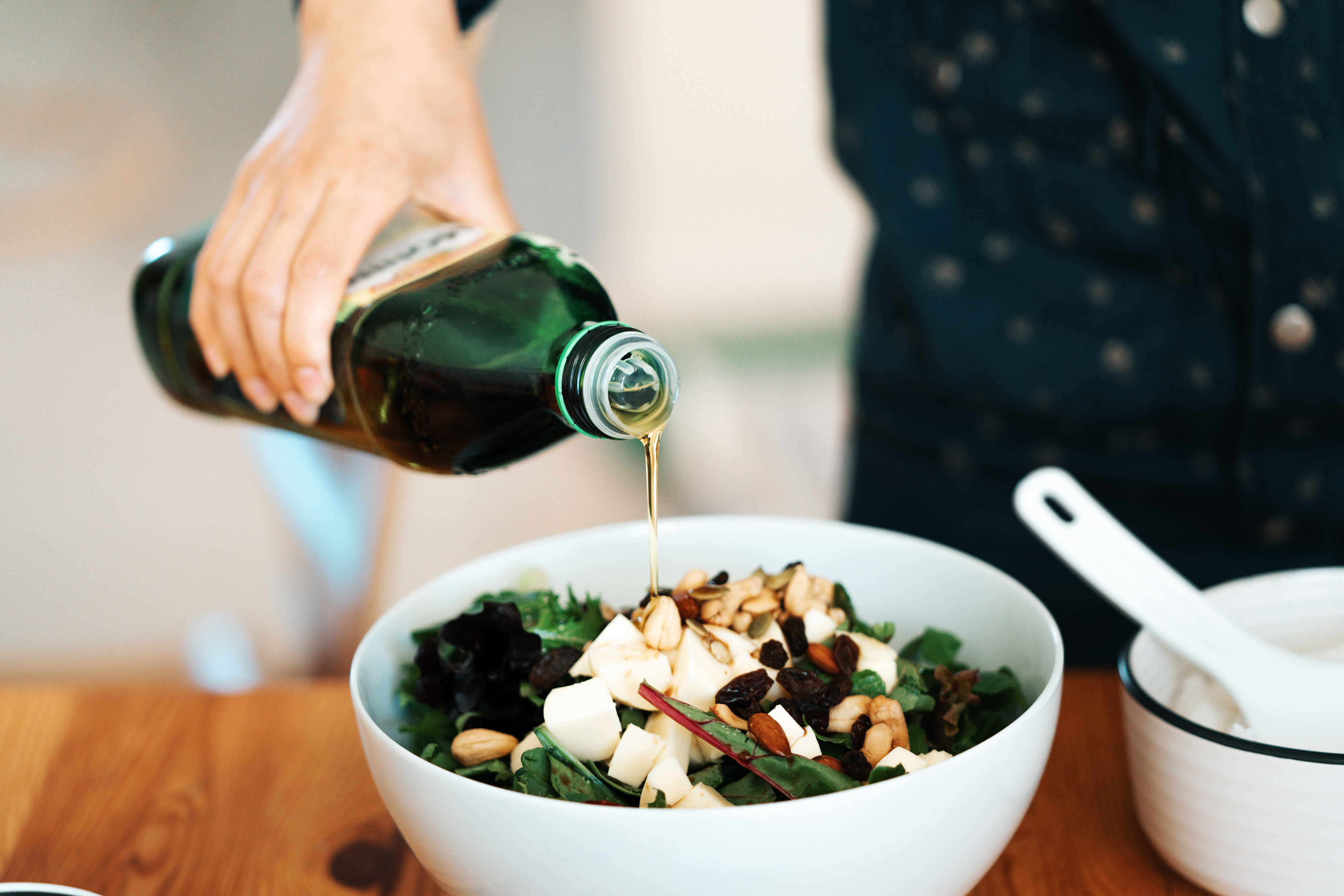 Person pouring olive oil on a salad with nuts and apples