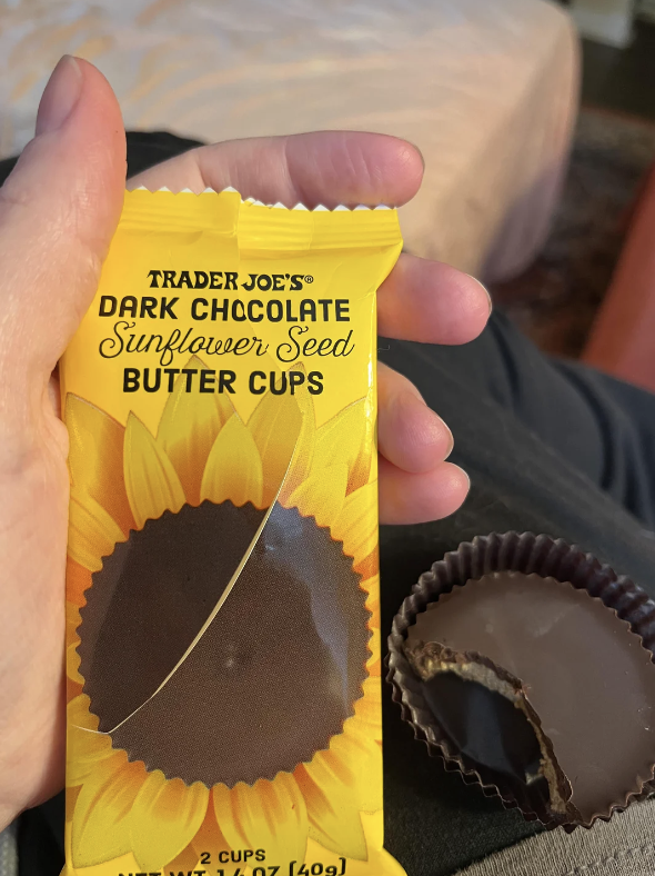 Hand holding Trader Joe&#x27;s Dark Chocolate Sunflower Seed Butter Cups with one unwrapped, showing filling