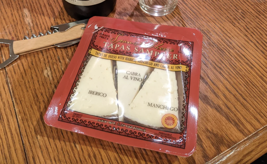 Package of Tapas Sampler with three types of cheese on a wooden table next to a corkscrew and bottle