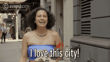 Woman in strapless top walks on street, laughing, with caption "I love this city!"